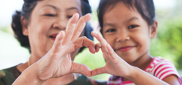 Elderly woman and young child making a heart shape with their hands